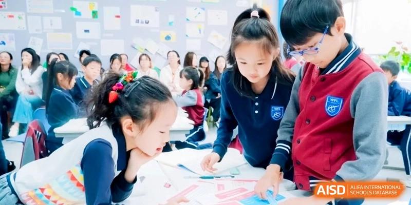 Group of students in navy blue uniforms working together on a collaborative paper-based project at a desk in a bright room at Shanghai Qingpu World Foreign Language High School.