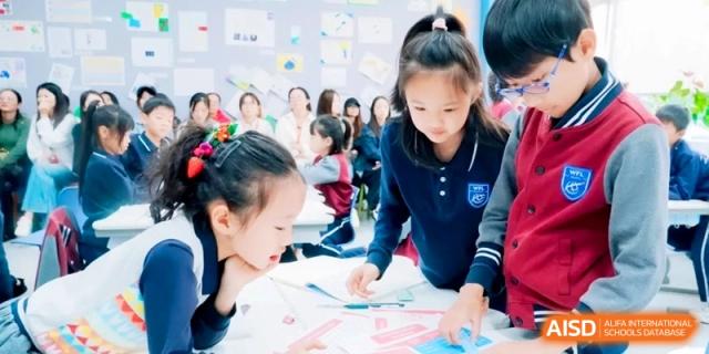Group of students in navy blue uniforms working together on a collaborative paper-based project at a desk in a bright room at Shanghai Qingpu World Foreign Language High School.