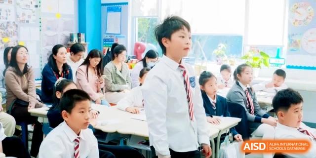 A young male student in a white shirt and striped tie stands up to participate in a classroom discussion at Shanghai Qingpu World Foreign Language High School.