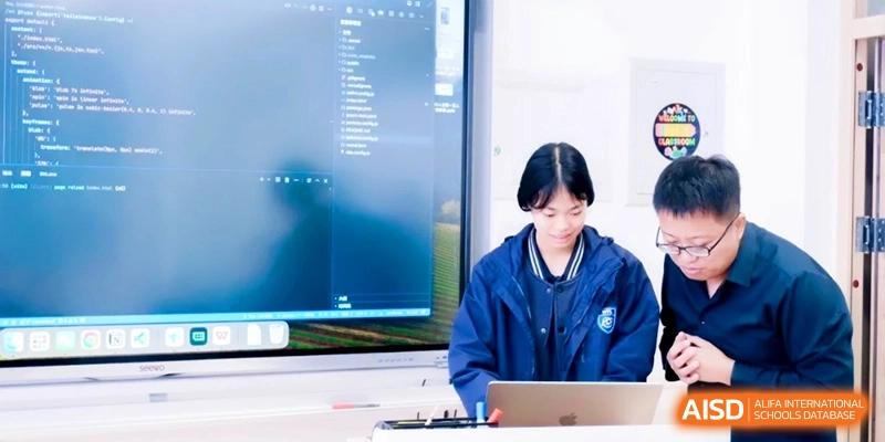 A student in a blue jacket sits in front of a large screen displaying computer code and file directories at Shanghai Qingpu World Foreign Language High School.