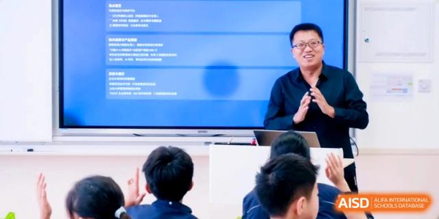 A male teacher presents a digital lesson on a large screen to a classroom of attentive students at Shanghai Qingpu World Foreign Language High School.
