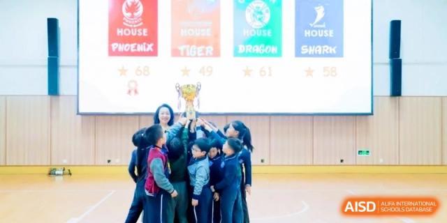 Group of students joyfully raising a gold trophy together during an indoor awards ceremony at Shanghai Qingpu World Foreign Language High School.