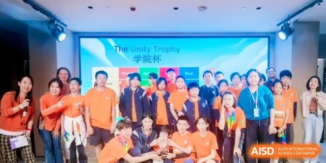 Students in orange uniforms posing together with a trophy for a group photo at Shanghai Qingpu World Foreign Language High School.