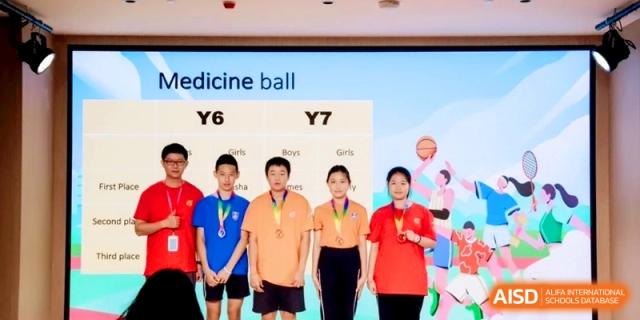 Five students wearing medals standing in front of a sports results screen for medicine ball at Shanghai Qingpu World Foreign Language High School.