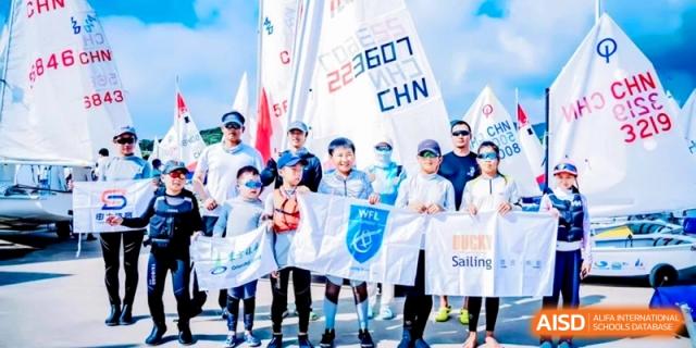 Group of students and coaches posing with sailing flags in front of sailboats at Shanghai Qingpu World Foreign Language High School.