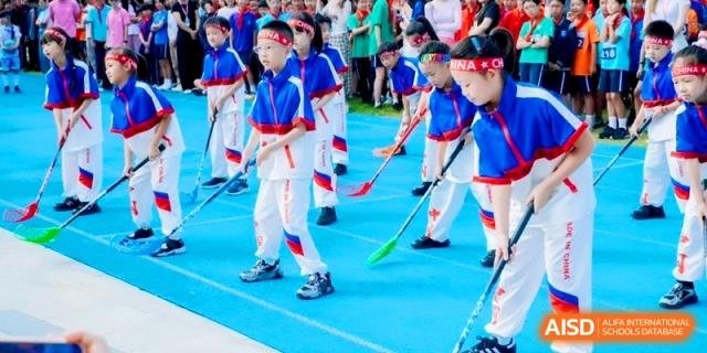 Young students practicing floor hockey in matching blue and white uniforms at Shanghai Qingpu World Foreign Language High School.