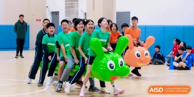 Students participating in a fun team-building race using large inflatable green toys at Shanghai Qingpu World Foreign Language High School.