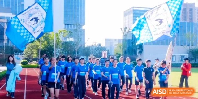 A large group of students in matching blue athletic shirts marches together outdoors during a school sports event at Shanghai Qingpu World Foreign Language High School.