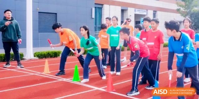 Students in colorful sports uniforms prepare for a relay race on a red running track behind orange and green cones at Shanghai Qingpu World Foreign Language High School.