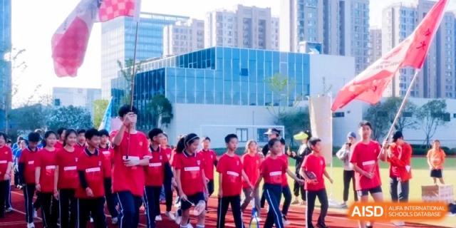 Students dressed in vibrant red athletic kits walk together in a coordinated group during an outdoor sports festival at Shanghai Qingpu World Foreign Language High School.