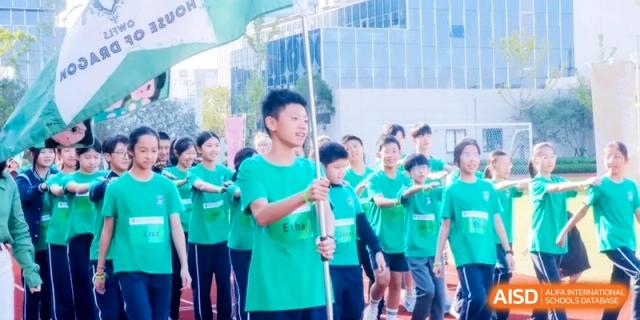 A student leader proudly carries a flag while leading a group of peers in green shirts across the athletic field at Shanghai Qingpu World Foreign Language High School.