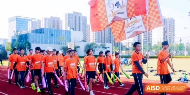 Students march in formation on the track carrying bright inflatable cheering sticks and large flags during a parade at Shanghai Qingpu World Foreign Language High School.