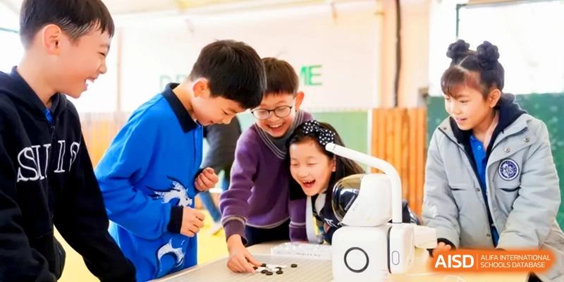 Three students laugh and play a board game with a small white robot in a bright classroom at Shanghai United International School, Hongqiao Campus.