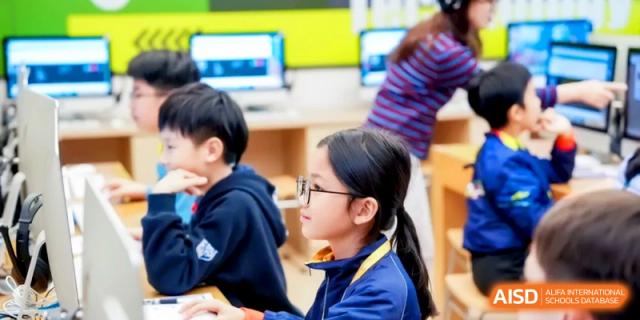 A young student with glasses focuses on a lesson in a modern, bright computer lab at Shanghai United International School, Hongqiao Campus.