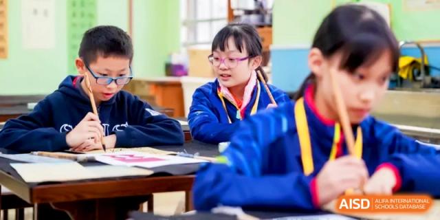 A young student in a blue uniform and glasses focuses on a group activity during a lesson at Shanghai United International School, Hongqiao Campus.