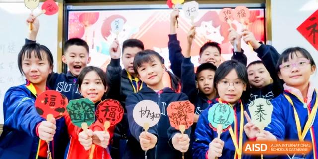 Excited students hold up traditional red and green Chinese cultural crafts in a group photo at Shanghai United International School, Hongqiao Campus.