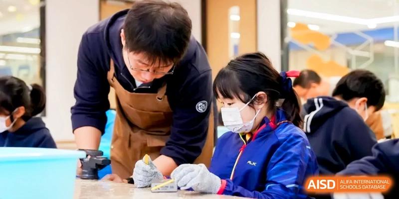 A student in a face mask works on a delicate craft project with a teacher's guidance at Shanghai United International School, Hongqiao Campus.