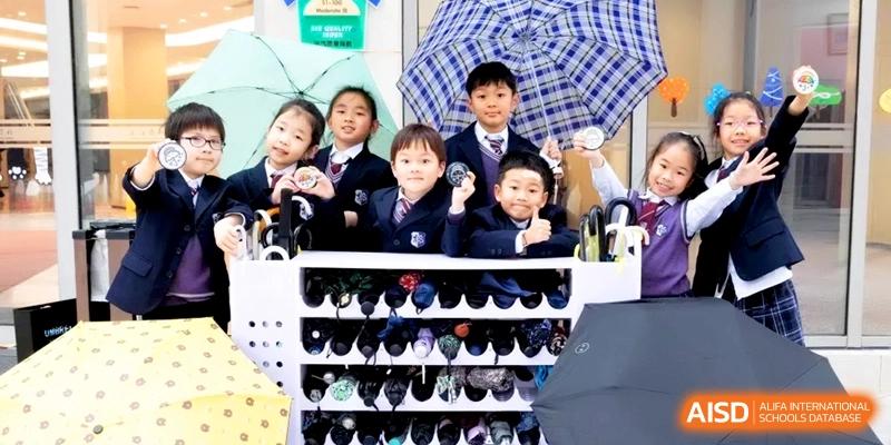 A group of four young students in smart uniforms poses together near a classroom cubby area at Shanghai United International School, Hongqiao Campus.