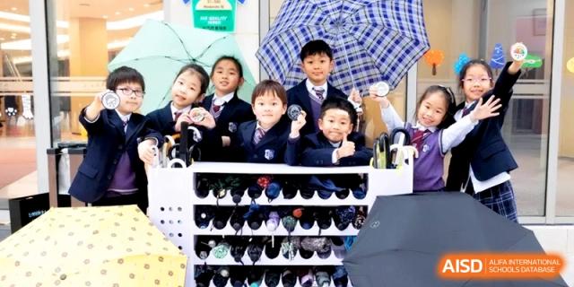A group of four young students in smart uniforms poses together near a classroom cubby area at Shanghai United International School, Hongqiao Campus.