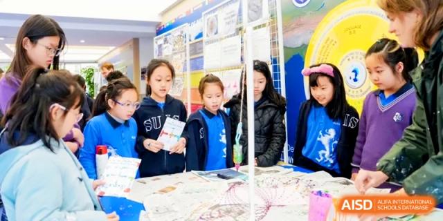 Students gather around a science project display with colorful charts and diagrams. | Shanghai United International School, Hongqiao Campus