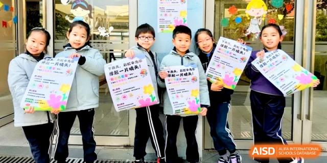 Three students proudly hold up colorful posters they created for a school project. | Shanghai United International School, Hongqiao Campus