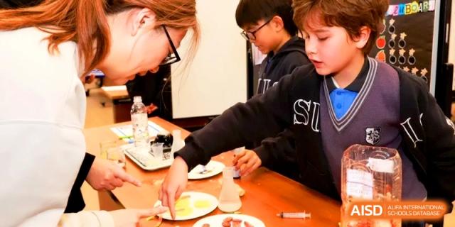 Students engage in a hands-on activity with small tools and materials on a classroom table. | Shanghai United International School, Hongqiao Campus