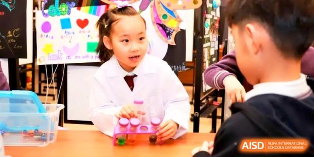 A young student in a white lab coat explores colorful liquids during a science fair. | Shanghai United International School, Hongqiao Campus