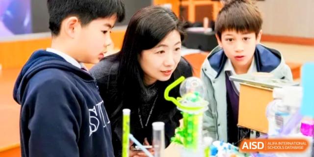 A teacher and students examine a glowing green science experiment in a darkened room. | Shanghai United International School, Hongqiao Campus