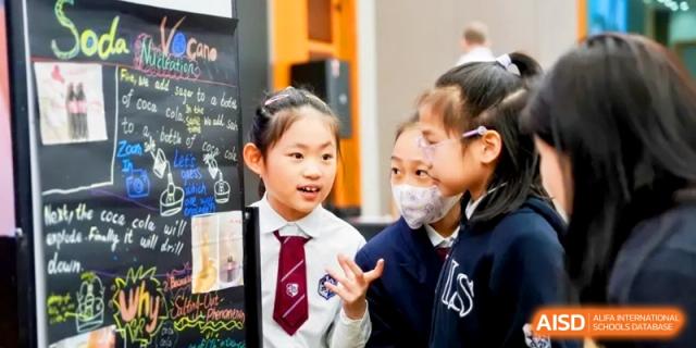 Students discuss a creative project displayed on a blackboard during a school event. | Shanghai United International School, Hongqiao Campus