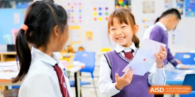 Smiling young female students in purple uniforms enjoy a lively classroom discussion with their teacher, showcasing the vibrant academic atmosphere at Shanghai United International School, Hongqiao Campus