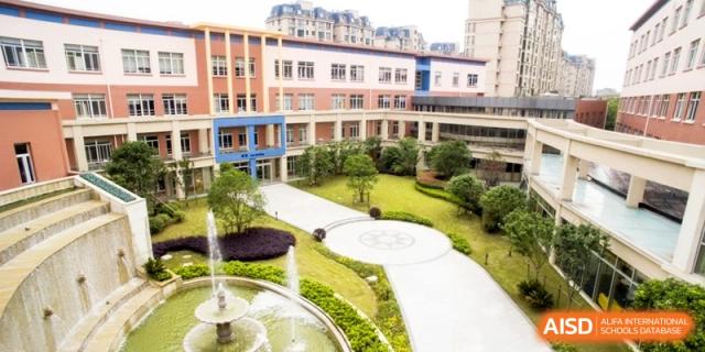 A high-angle view of the modern school courtyard featuring manicured green gardens, a fountain, and architectural pathways at Shanghai United International School, Hongqiao Campus