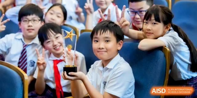 A student smiles proudly while holding a gold star trophy for an academic achievement. | Shanghai United International School, Hongqiao Campus