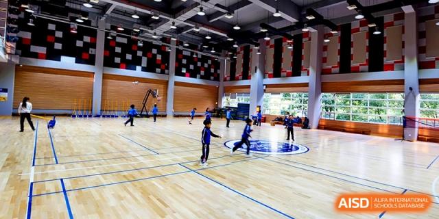 Students participate in physical education and sports activities on the polished wood floor of a large, well-lit indoor gymnasium at Shanghai United International School, Hongqiao Campus