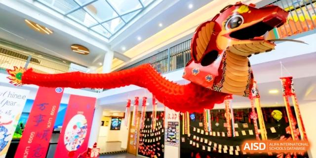 A large traditional red dragon decoration hangs from the ceiling in a brightly lit school hallway at Shanghai United International School, Hongqiao Campus