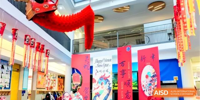 Festive Chinese New Year banners and a hanging red dragon decorate the modern atrium of Shanghai United International School, Hongqiao Campus