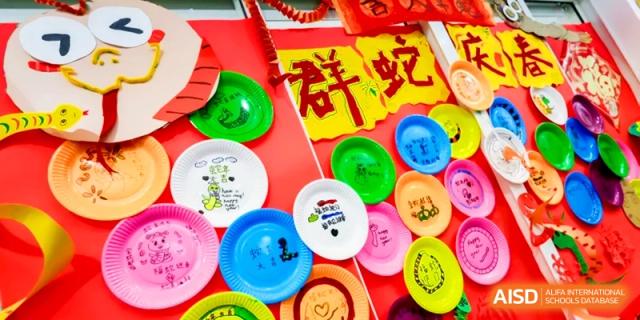 Decorative colorful paper plates with hand-drawn designs are displayed on a red wall at Shanghai United International School, Hongqiao Campus