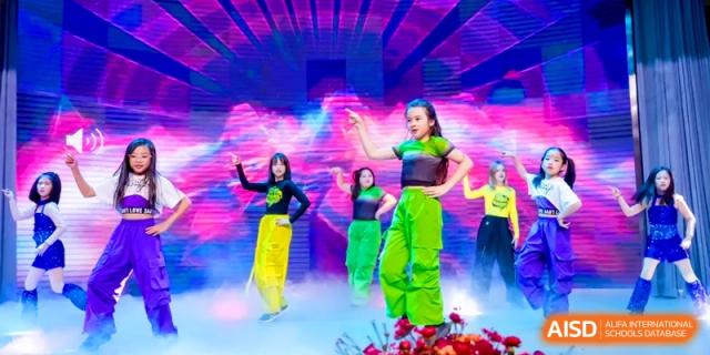 Student performers in bright costumes dance on a foggy stage during a vibrant school showcase at Shanghai United International School, Hongqiao Campus