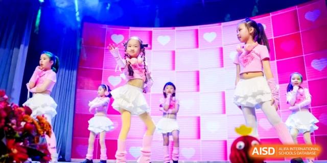 Young students in pink and white outfits perform a choreographed dance on a stage with heart motifs at Shanghai United International School, Hongqiao Campus