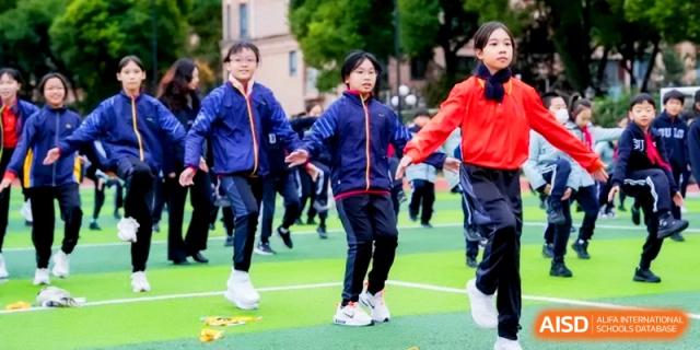 Students in blue and red athletic jackets participate in an organized outdoor activity on the field at Shanghai United International School, Hongqiao Campus