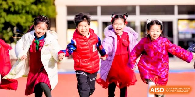 Two young children in warm winter jackets hold hands and run happily across the school grounds at Shanghai United International School, Hongqiao Campus
