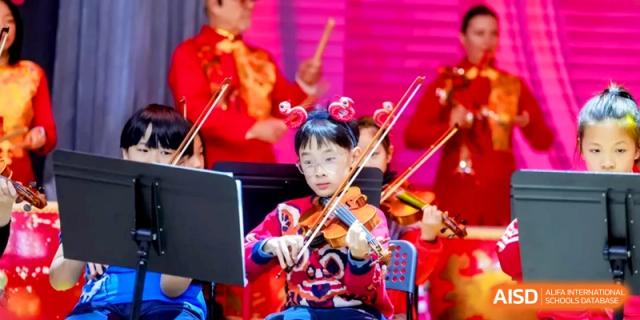 A student musician focuses on playing the violin during a festive school orchestral performance at Shanghai United International School, Hongqiao Campus