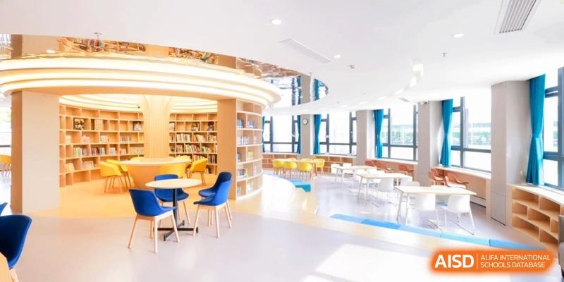 A modern school library features curved wooden bookshelves and colorful seating areas with large windows at Shanghai United International School, Pudong.