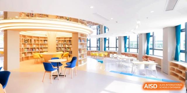 A modern school library features curved wooden bookshelves and colorful seating areas with large windows at Shanghai United International School, Pudong.