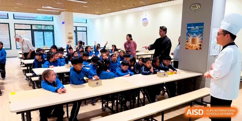 Students in blue uniforms sit at desks in a bright classroom while a teacher addresses the group during a lesson at Shanghai United International School, Pudong.
