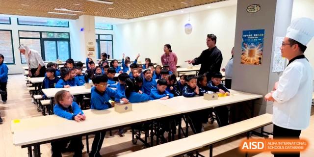 Students in blue uniforms sit at desks in a bright classroom while a teacher addresses the group during a lesson at Shanghai United International School, Pudong.
