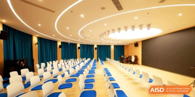 Rows of blue and white chairs are neatly arranged in a spacious auditorium with elegant curved ceiling lights at Shanghai United International School, Pudong.
