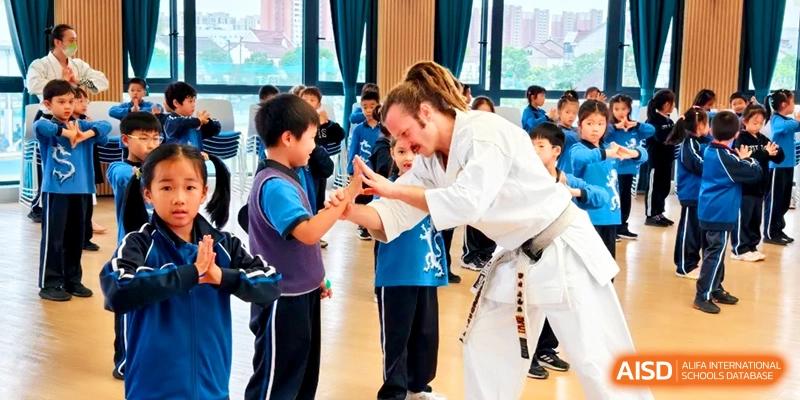 A martial arts instructor in a white gi teaching a young student a technique at Shanghai United International School, Pudong