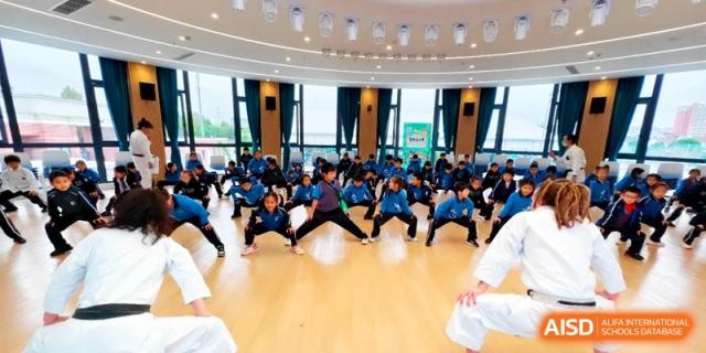 Students practicing martial arts stances together in a spacious wooden hall at Shanghai United International School, Pudong