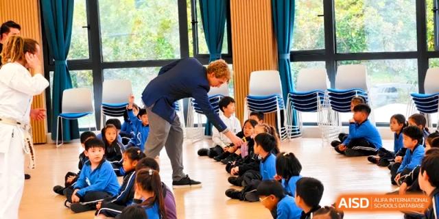 A teacher leaning down to interact with students sitting on the floor at Shanghai United International School, Pudong