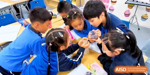 Students gather around a table to observe a science experiment with beakers and liquids in a classroom at Shanghai United International School, Pudong